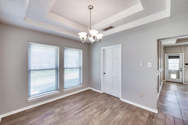 unfurnished room with a tray ceiling, a wealth of natural light, hardwood / wood-style floors, and a chandelier