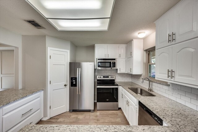 kitchen featuring light stone countertops, sink, stainless steel appliances, light hardwood / wood-style flooring, and white cabinets