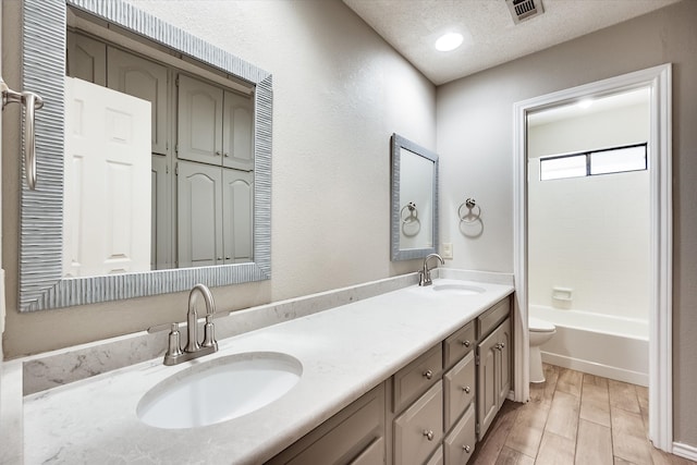 full bathroom with hardwood / wood-style floors, vanity, washtub / shower combination, toilet, and a textured ceiling