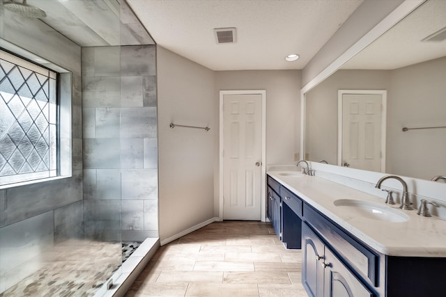 bathroom with a textured ceiling, vanity, tiled shower, and a wealth of natural light