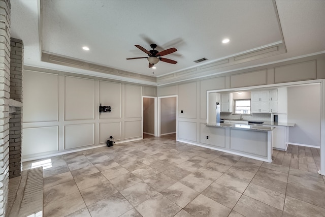 interior space with kitchen peninsula, a tray ceiling, ceiling fan, and ornamental molding