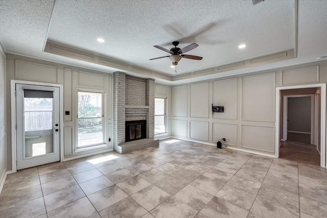 unfurnished living room featuring a textured ceiling, ceiling fan, a raised ceiling, and a fireplace