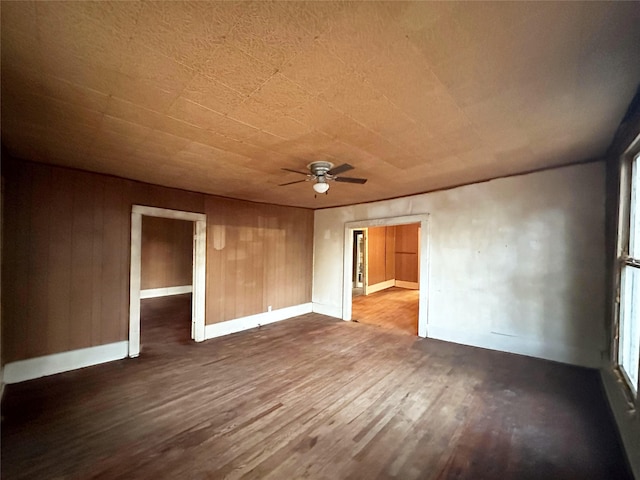 spare room with ceiling fan, wood walls, and dark wood-type flooring