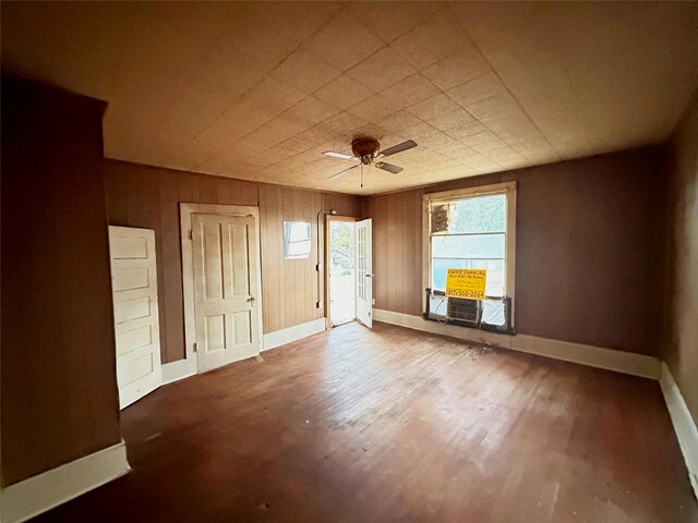 spare room featuring ceiling fan, cooling unit, wood-type flooring, and wooden walls