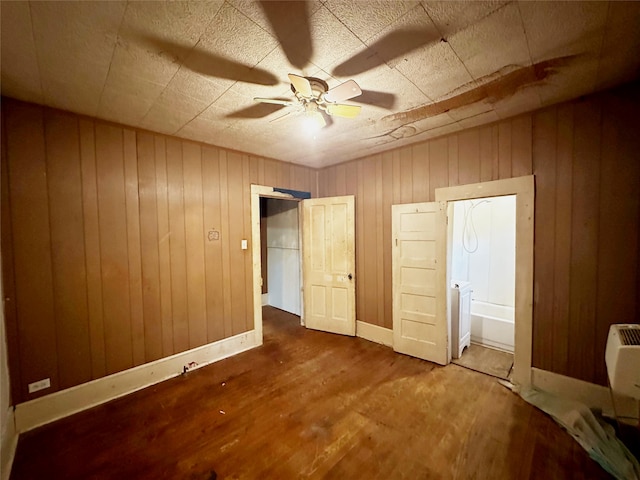 unfurnished bedroom featuring ceiling fan, wooden walls, ensuite bathroom, and hardwood / wood-style flooring