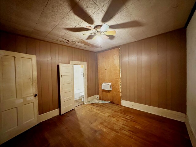 unfurnished bedroom with hardwood / wood-style floors, ensuite bathroom, ceiling fan, and wooden walls