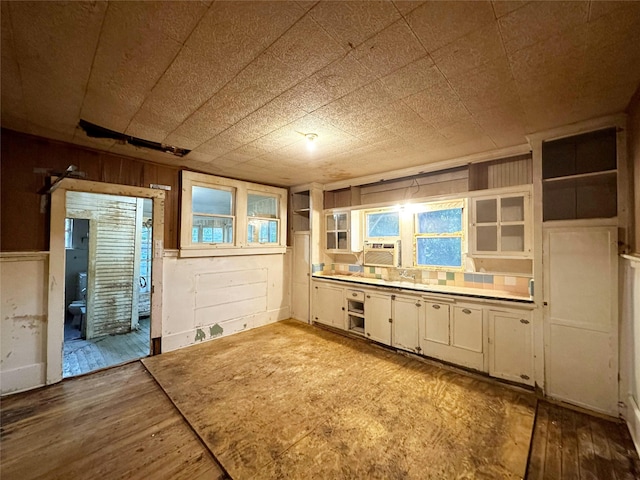 kitchen featuring white cabinets, light hardwood / wood-style flooring, cooling unit, and wood walls