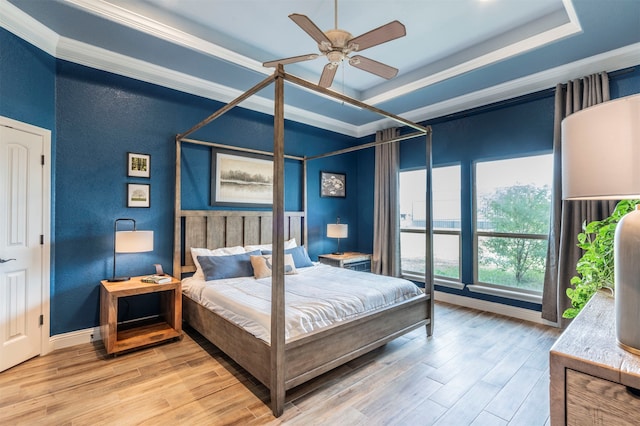 bedroom featuring ceiling fan, wood-type flooring, crown molding, and a tray ceiling