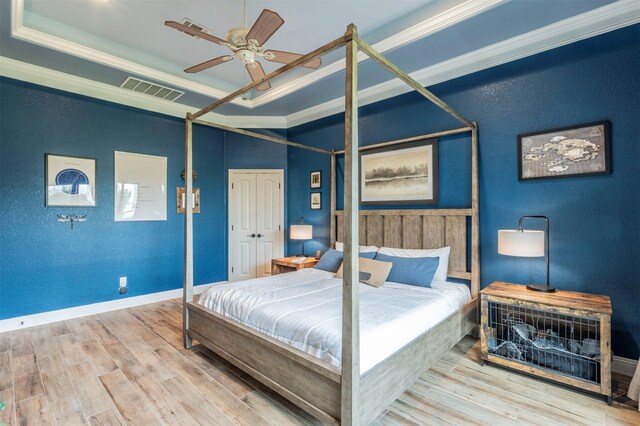 bedroom featuring hardwood / wood-style floors, a raised ceiling, crown molding, ceiling fan, and a closet