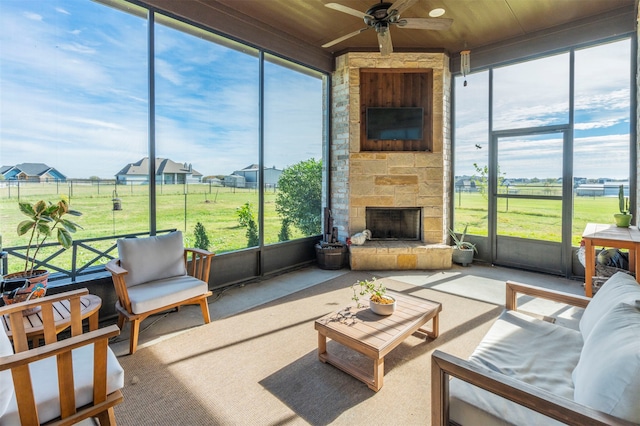 sunroom / solarium with ceiling fan, a healthy amount of sunlight, a stone fireplace, and wood ceiling