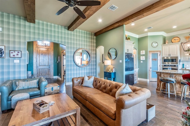 living room featuring ceiling fan with notable chandelier, beam ceiling, ornamental molding, and dark wood-type flooring