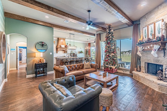 living room with beam ceiling, ceiling fan, a stone fireplace, and dark hardwood / wood-style flooring