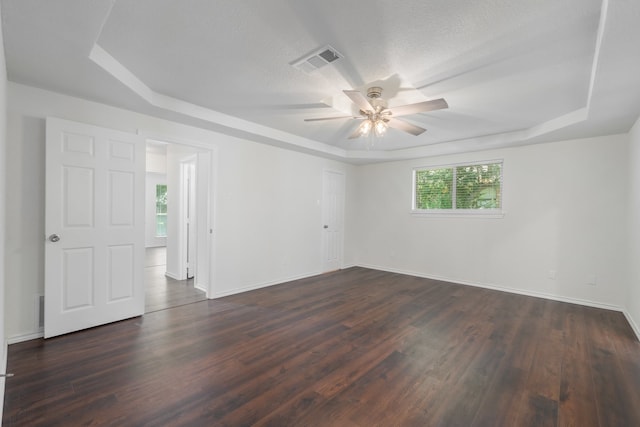 empty room with a raised ceiling, ceiling fan, dark wood-type flooring, and a textured ceiling