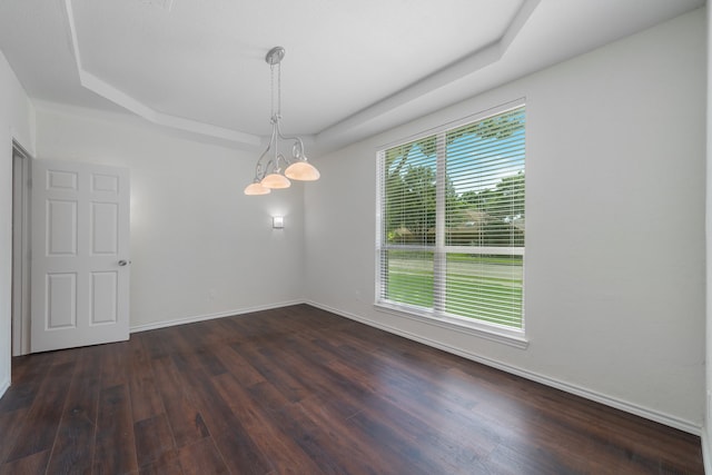 empty room featuring a raised ceiling, dark hardwood / wood-style floors, and an inviting chandelier