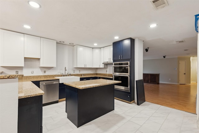 kitchen with light stone counters, a kitchen island, visible vents, a sink, and appliances with stainless steel finishes