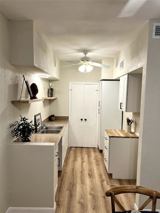 kitchen with a textured ceiling, sink, light hardwood / wood-style flooring, white cabinetry, and butcher block counters