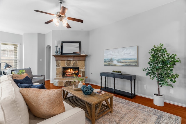 living room with hardwood / wood-style flooring, a stone fireplace, and ceiling fan