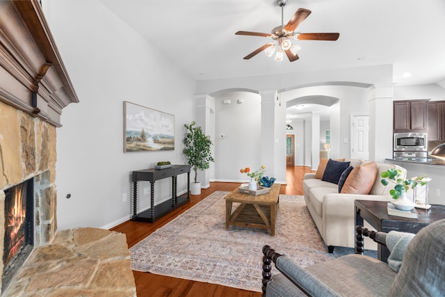 living room with a stone fireplace, ceiling fan, and light wood-type flooring