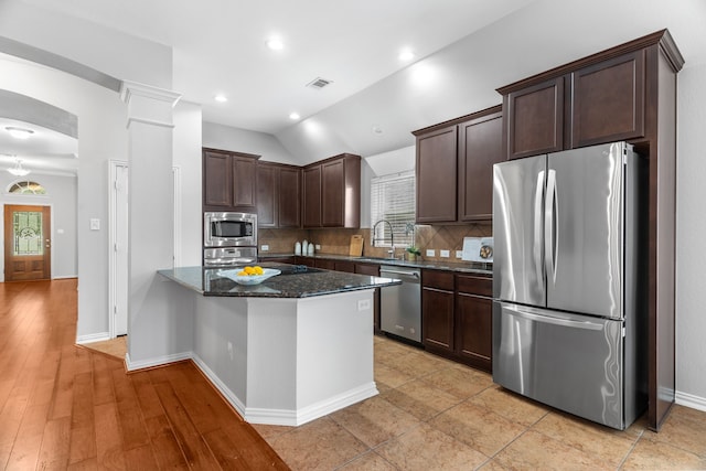 kitchen with lofted ceiling, dark stone counters, sink, light hardwood / wood-style floors, and stainless steel appliances