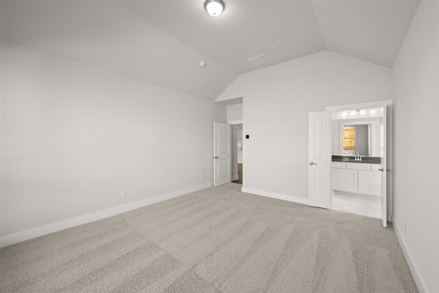 unfurnished bedroom with ensuite bathroom, sink, light colored carpet, and lofted ceiling