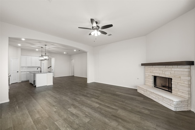 unfurnished living room with ceiling fan, sink, dark hardwood / wood-style flooring, and a stone fireplace