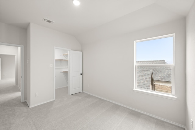 unfurnished bedroom featuring a walk in closet, light carpet, multiple windows, and a closet