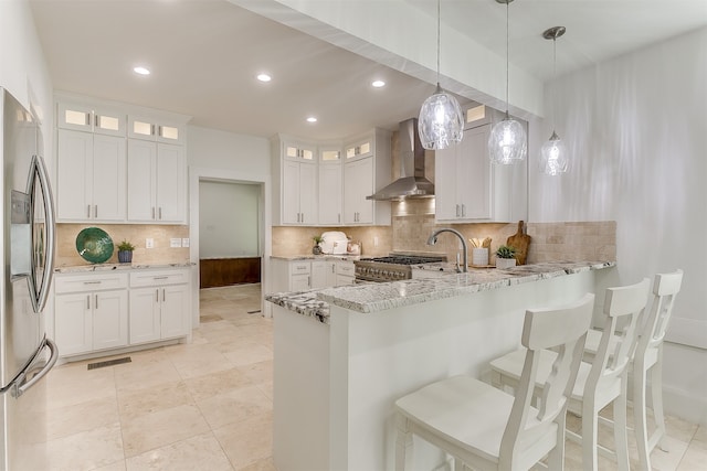 kitchen with white cabinets, light stone countertops, wall chimney exhaust hood, and appliances with stainless steel finishes