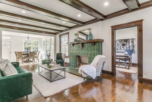 living room featuring crown molding, wood-type flooring, beam ceiling, a notable chandelier, and a tiled fireplace