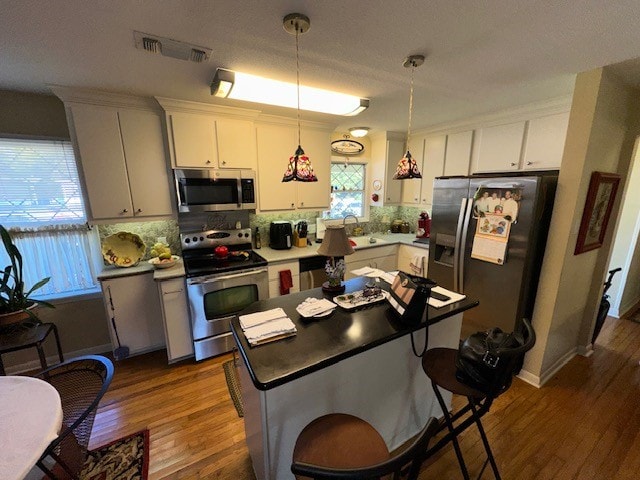 kitchen featuring backsplash, white cabinets, hardwood / wood-style flooring, decorative light fixtures, and stainless steel appliances