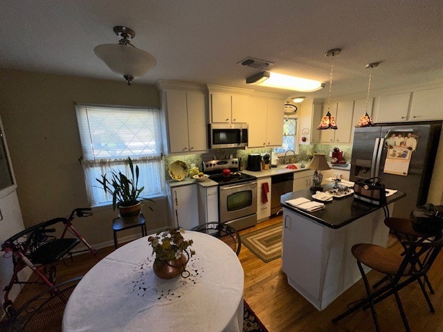 kitchen featuring white cabinets, hanging light fixtures, hardwood / wood-style flooring, appliances with stainless steel finishes, and a kitchen island