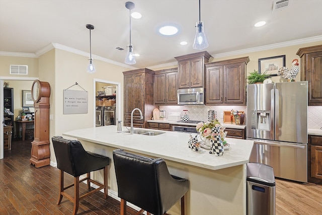 kitchen with stainless steel appliances, a kitchen island with sink, sink, hardwood / wood-style floors, and washing machine and dryer