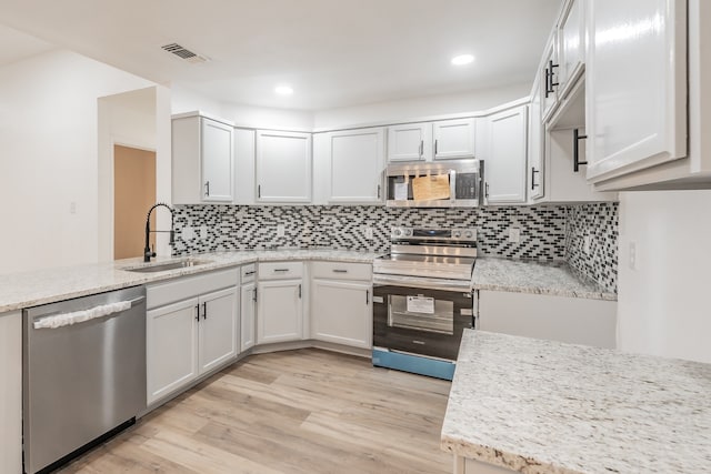 kitchen featuring light wood-type flooring, light stone counters, stainless steel appliances, sink, and white cabinets