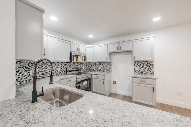 kitchen featuring sink, stainless steel appliances, tasteful backsplash, light stone counters, and light hardwood / wood-style flooring