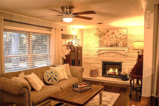 living room with a stone fireplace, dark hardwood / wood-style floors, and ceiling fan