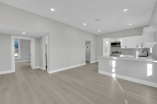 kitchen with white cabinetry, sink, stainless steel appliances, kitchen peninsula, and light wood-type flooring