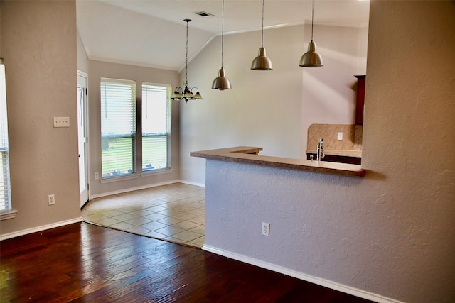 kitchen with tasteful backsplash, ornamental molding, vaulted ceiling, wood-type flooring, and hanging light fixtures