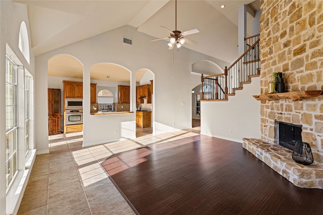 unfurnished living room with a stone fireplace, ceiling fan, light hardwood / wood-style flooring, and high vaulted ceiling