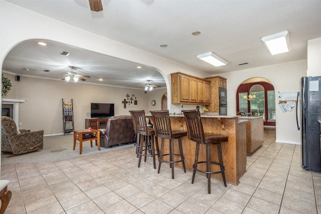 kitchen featuring black appliances, light tile patterned floors, a fireplace, ornamental molding, and a breakfast bar area