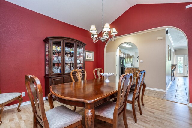 dining space with light wood-type flooring, vaulted ceiling, and a notable chandelier