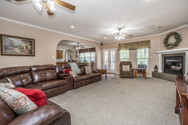 carpeted living room featuring french doors, plenty of natural light, crown molding, and a tiled fireplace