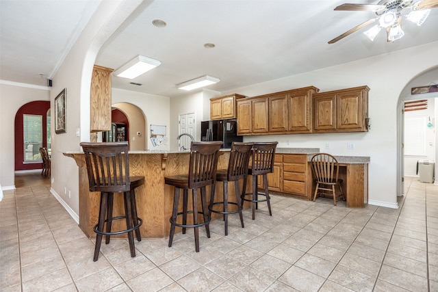 kitchen with black fridge, kitchen peninsula, crown molding, a kitchen bar, and light tile patterned floors