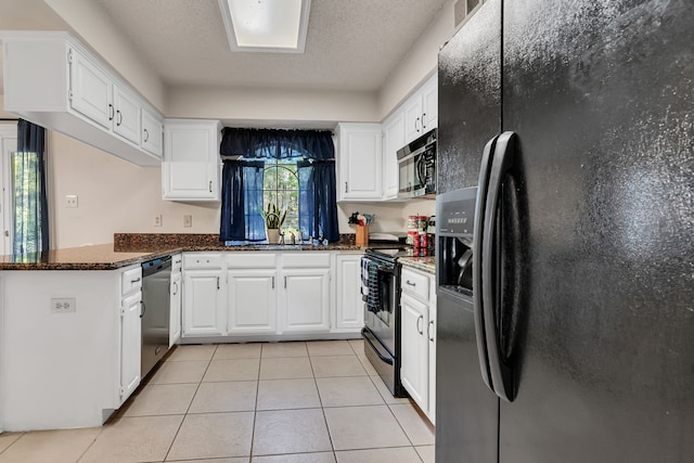 kitchen with black appliances, kitchen peninsula, dark stone countertops, light tile patterned floors, and white cabinetry