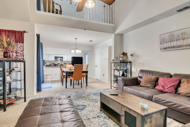 living room with a textured ceiling, ceiling fan with notable chandelier, and light tile patterned floors