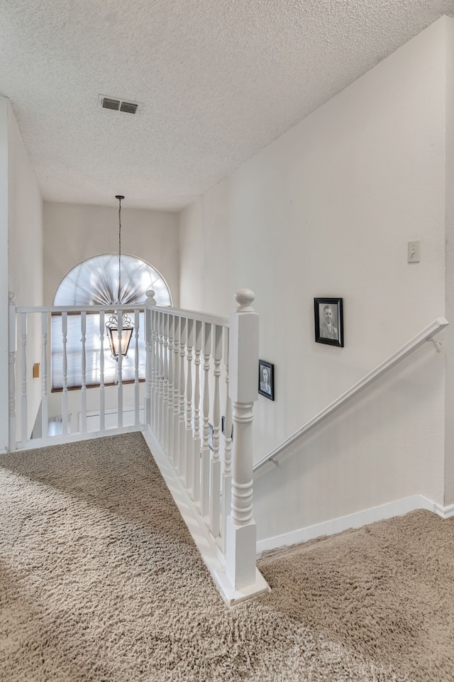 corridor with an inviting chandelier, carpet floors, and a textured ceiling