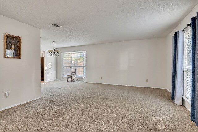 unfurnished room featuring light carpet, a textured ceiling, and a notable chandelier