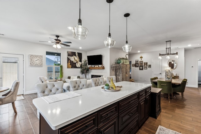 kitchen with ceiling fan, light wood-type flooring, decorative light fixtures, a kitchen island, and dark brown cabinetry