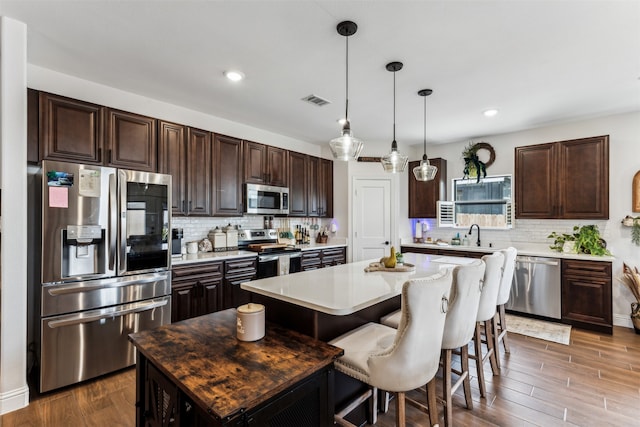 kitchen featuring a center island, dark wood-type flooring, hanging light fixtures, dark brown cabinets, and stainless steel appliances