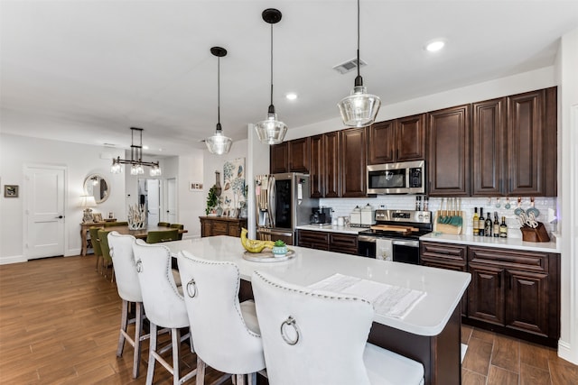 kitchen featuring appliances with stainless steel finishes, dark hardwood / wood-style flooring, decorative light fixtures, and a kitchen island