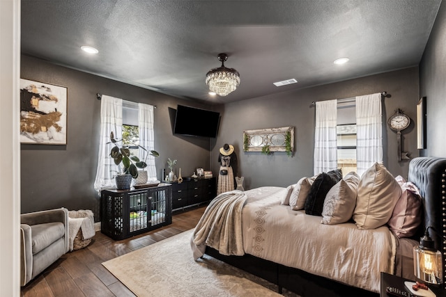 bedroom with a chandelier, a textured ceiling, and dark wood-type flooring