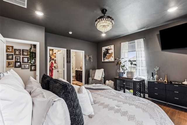 bedroom with ensuite bathroom, a notable chandelier, and hardwood / wood-style flooring